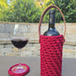 Handmade crochet wine holder with leather handle displayed outdoors beside a glass of red wine – eco-friendly gift for wine lovers.