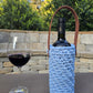 Handmade crochet wine holder with leather handle displayed outdoors beside a glass of red wine – eco-friendly gift for wine lovers.