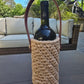 Handmade crochet wine holder with leather handle displayed outdoors beside a glass of red wine – eco-friendly gift for wine lovers.