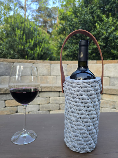 Handmade crochet wine holder with leather handle displayed outdoors beside a glass of red wine – sustainable gift for wine lovers.