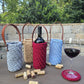 Handmade crochet wine holder with leather handle displayed outdoors beside a glass of red wine – eco-friendly gift.