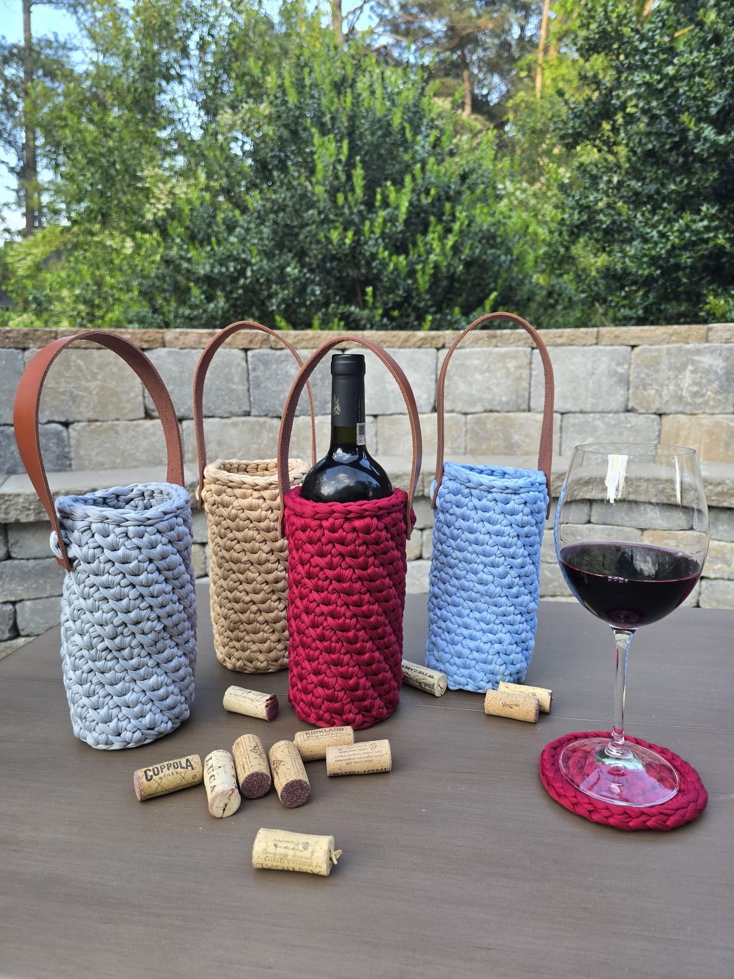 Handmade crochet wine holder with leather handle displayed outdoors beside a glass of red wine – eco-friendly gift.