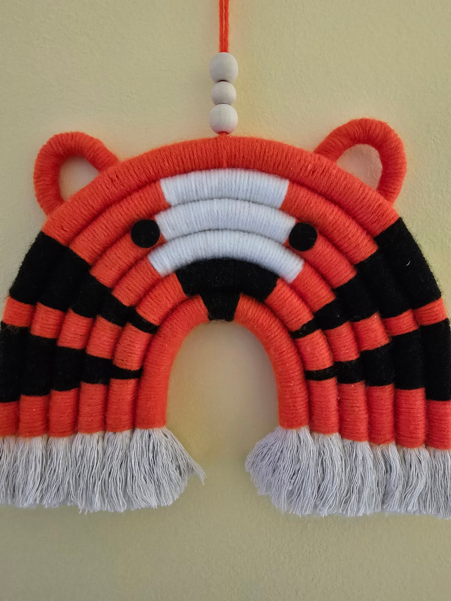Close-up detail of handmade tiger rainbow wall hanging showing cotton cord texture and bright orange color.